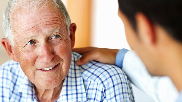 Photo of a senior patient with hand of a clinician on his shoulder